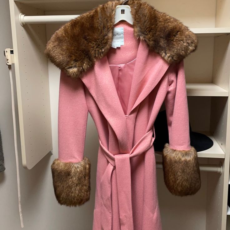 a pink coat with fur collar and cuffs hanging on a white shelf in a closet