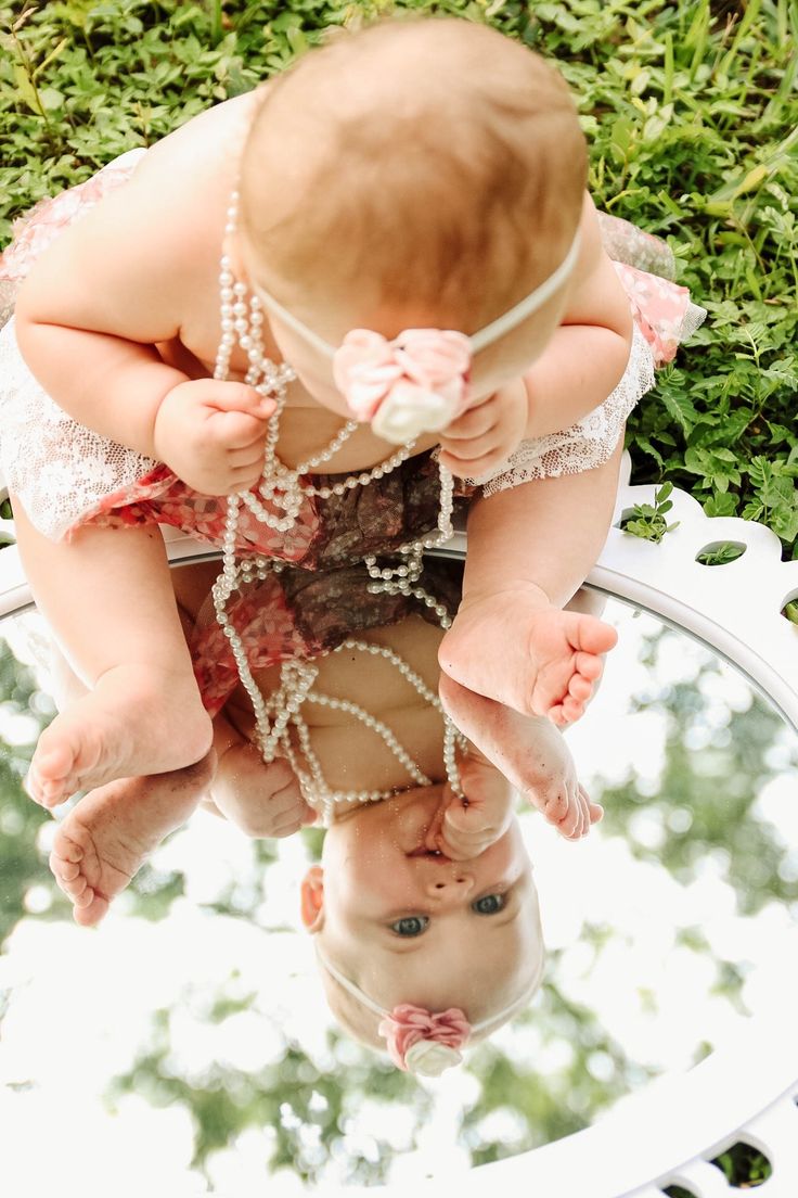 a baby in a dress looking at herself in the mirror