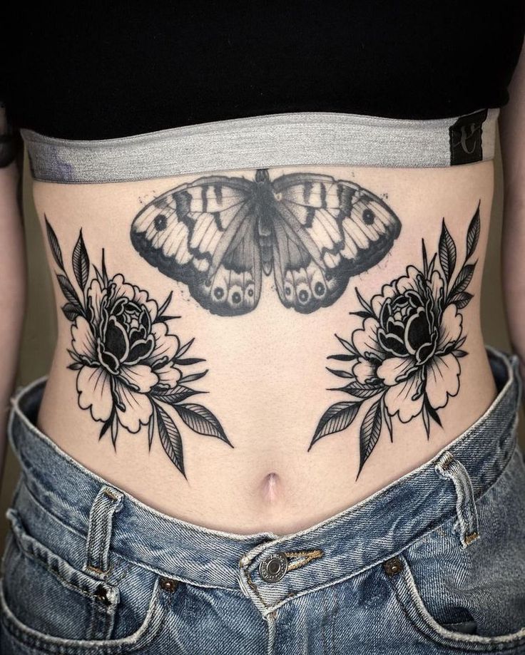 a woman's stomach with a butterfly and flowers tattoo on her belly, which is black and white