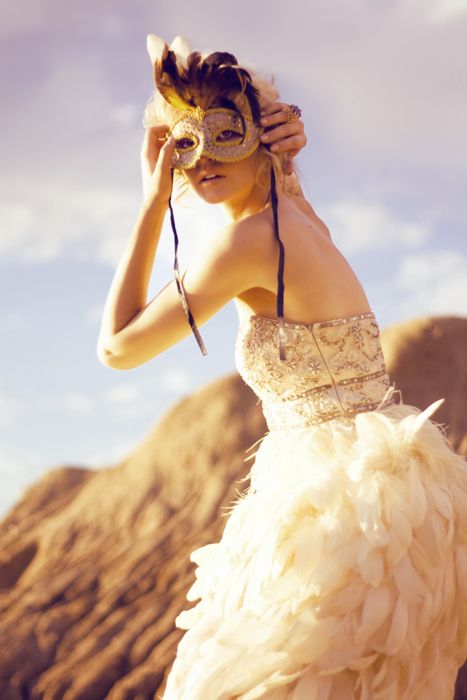 a woman in a white dress with a mask on her head and feathers around her neck