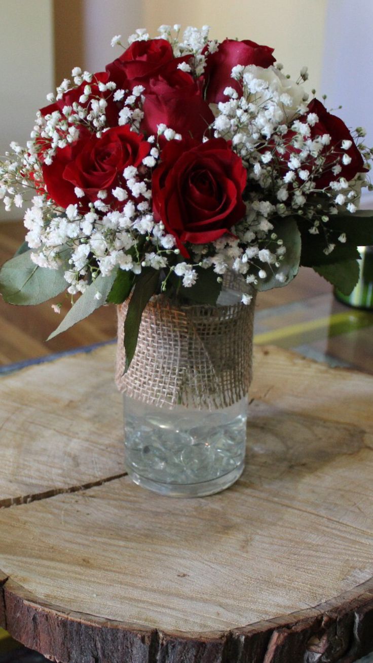 a vase filled with red roses sitting on top of a wooden table covered in burlock