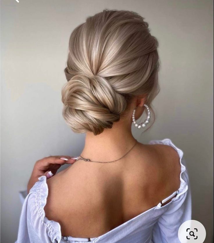 a woman with blonde hair in a low bun updo and pearls on her necklace