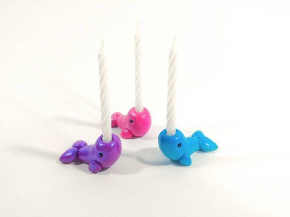 three candles are shaped like dolphins and one is pink, blue, and purple with white sticks sticking out of it