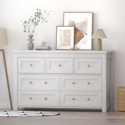 a white dresser sitting next to a lamp on top of a hard wood floor