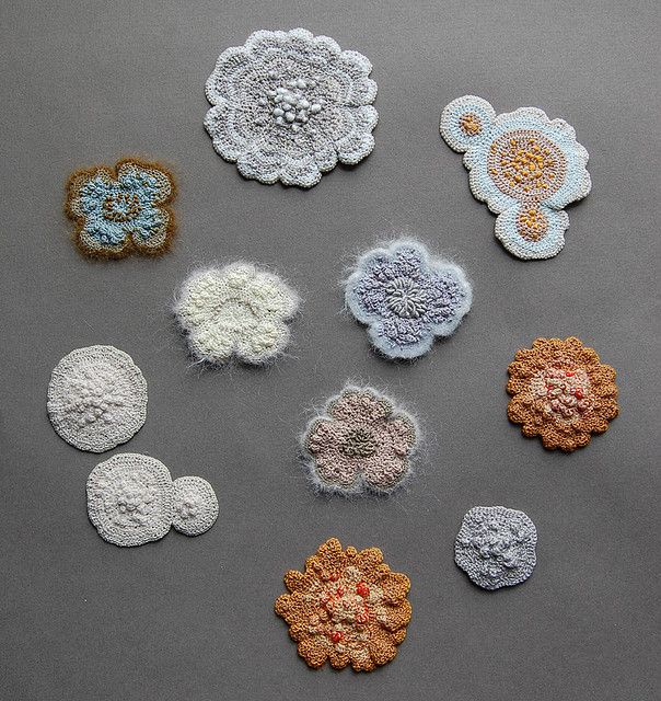 nine crocheted flower appliques are arranged on a gray surface, one is white and the other is orange