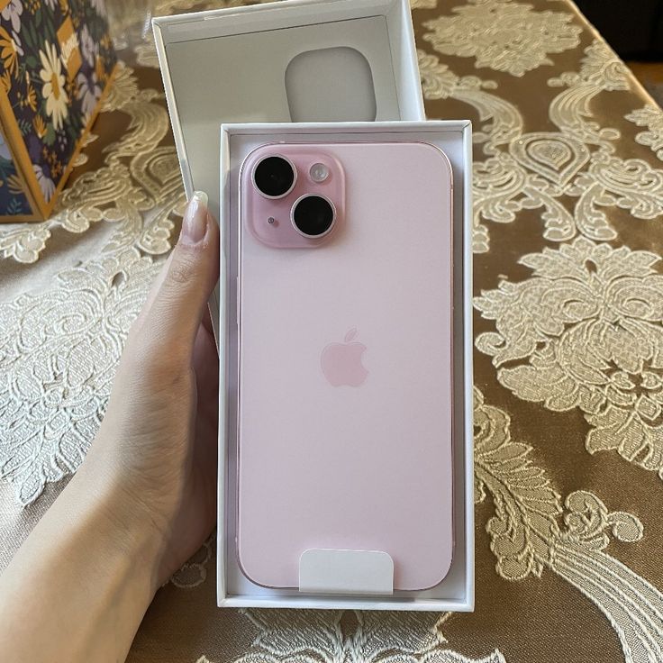 a pink iphone case sitting in a box on a table next to a person's hand