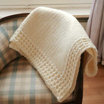 a white knitted blanket sitting on top of a chair next to a window sill