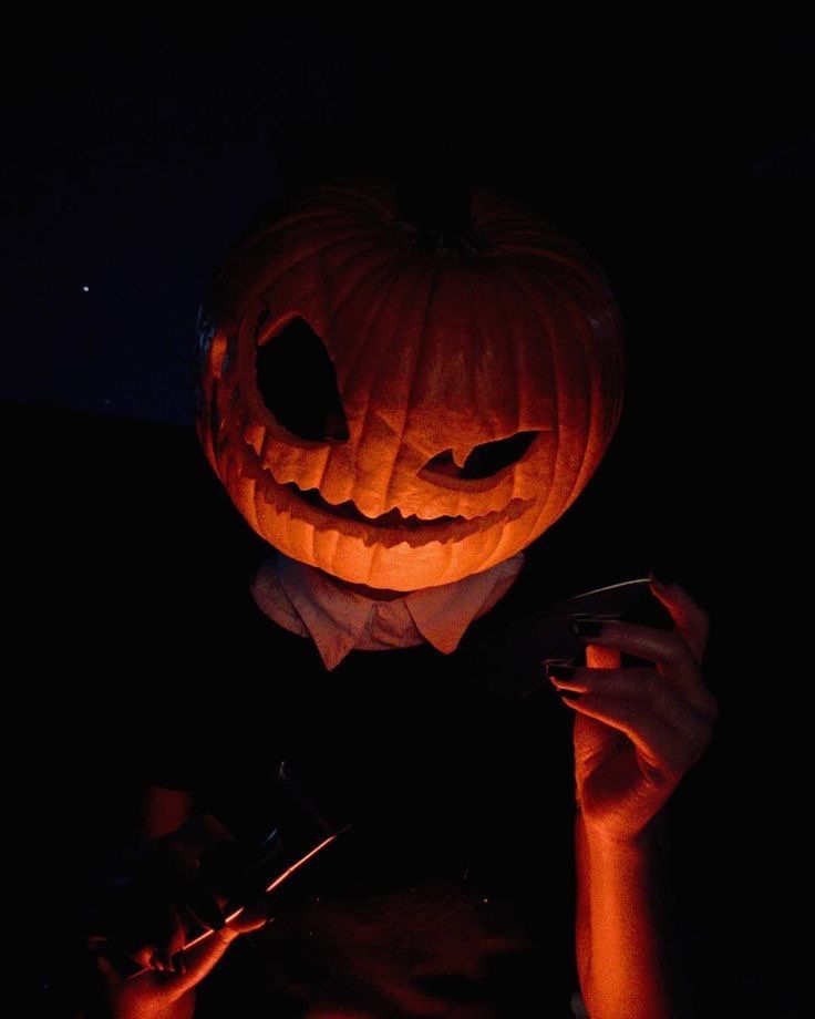 a person holding a cell phone in front of a carved pumpkin