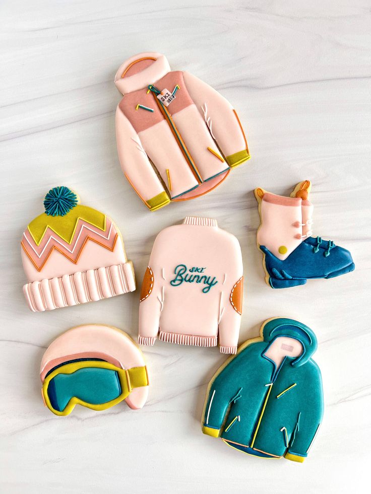 decorated cookies in the shape of sweaters and ski goggles on a white surface