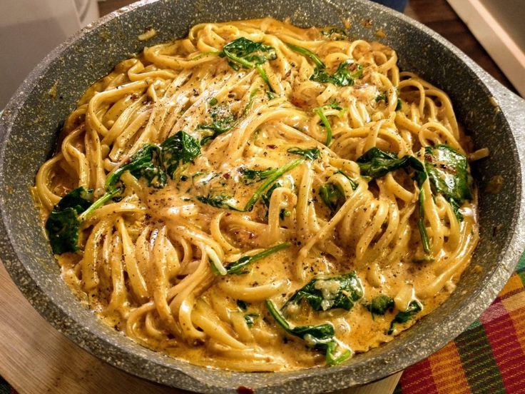 a bowl filled with pasta and spinach on top of a table