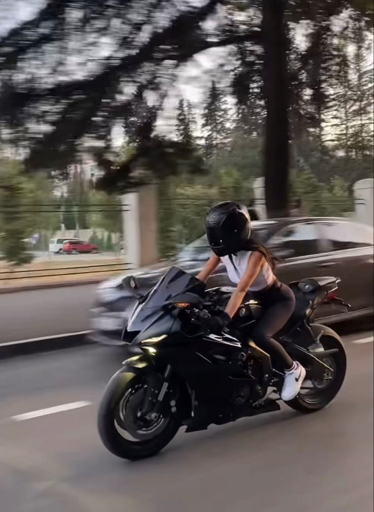 a woman riding on the back of a black motorcycle down a street next to a car