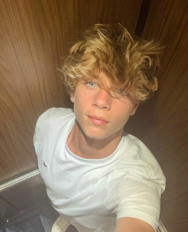 a young man with blonde hair sitting in front of a door