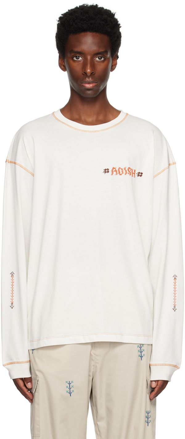 Cotton jersey T-shirt. · Rib knit crewneck and cuffs · Hand-stitched tatreez logo at chest · Hand-stitched tatreez detailing at sleeves · Logo patch at back collar · Textile patch at back hem · Contrast stitching in orange Supplier color: Off white White T-shirt With Ribbed Cuffs For Spring, White Embroidered T-shirt For Fall, White T-shirt With Embroidered Text For Fall, White Sweatshirt With Embroidered Graphics, White Long Sleeve T-shirt With Embroidered Logo, White Relaxed Fit Sweatshirt With Embroidered Graphics, White Crew Neck T-shirt For Spring, White Casual Tops With Contrast Stitching, White Embroidered Sweatshirt With Relaxed Fit