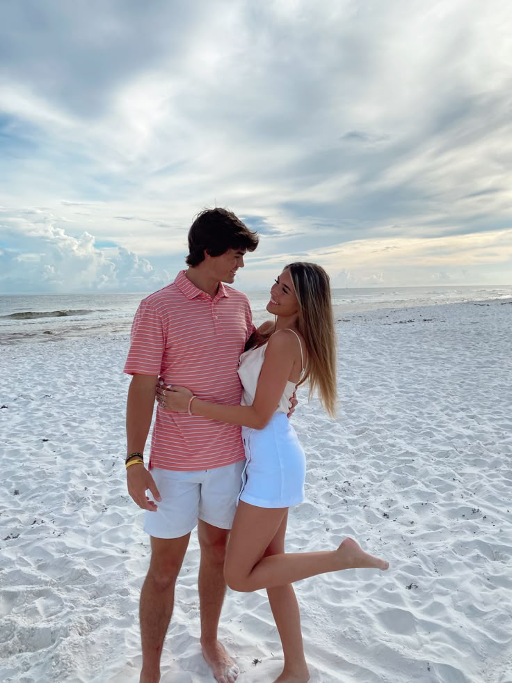 a man and woman are standing in the sand at the beach with their arms around each other