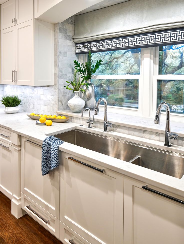 a kitchen with white cabinets and stainless steel sink, dishwasher and window in the background