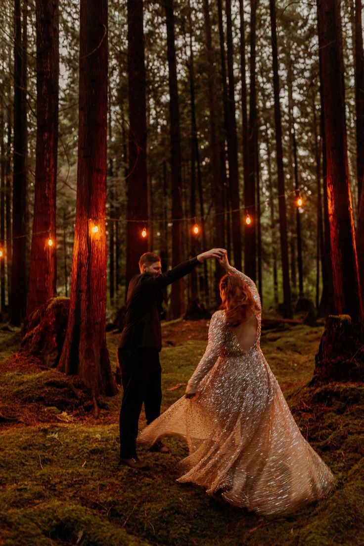 a bride and groom dancing in the woods at their outdoor wedding reception with string lights