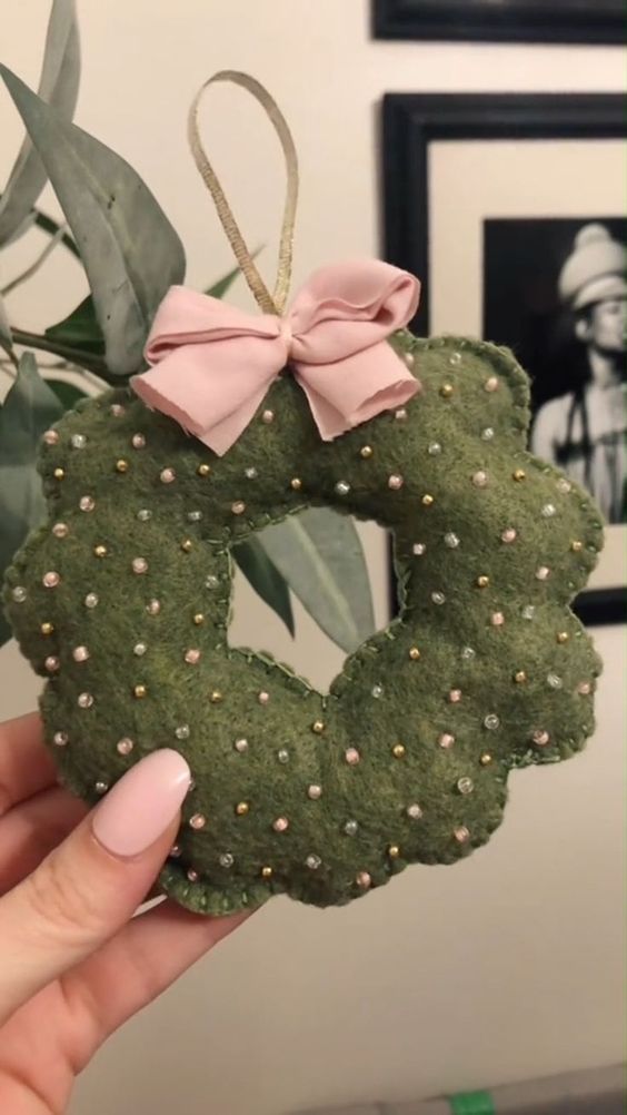 a hand holding a green wreath ornament with pink bows