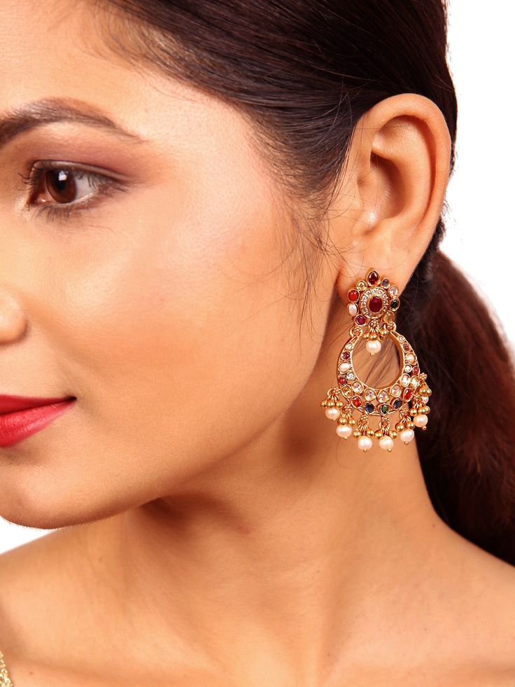 Our latest Anvi Chaandbali earring is a testament to intricate design and meticulous craftsmanship. It features a distinctive tilak stud, with a small pearl and ball drop delicately positioned at the center of the Chandbali, drawing attention to its unique charm. Adorned with Navarathna gemstones (Ruby, pearl, green emerald, red coral, blue sapphire, yellow sapphire, white zircon, moonstone & Hessonite) to this earring radiates elegance. The addition of graceful ball dangles and pearls adds the Fusion Kundan Danglers With Pearl Drop, Fusion Style Pearl Earrings With Meenakari For Celebration, Fusion Style Kundan Chandbalis With Pearl Drop, Fusion Pearl Earrings With Meenakari For Celebrations, Fusion Style Festive Chandbalis For Pierced Ears, Festive Fusion Pearl Earrings With Intricate Design, Festive Fusion Pearl Earrings For Festivals, Fusion Style Kundan Jhumkas With Pearl Drop, Fusion Style Chandbali Pearl Earrings With Meenakari