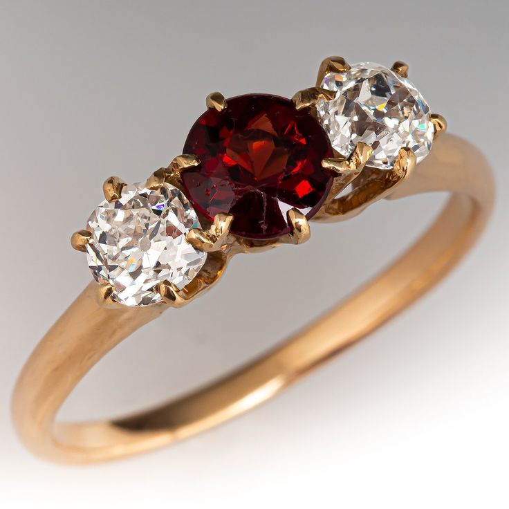 This vintage three-stone ring is centered with one (1) round natural garnet in a six-prong setting. On either side of center is one (1) old European cut diamond in a shared six -prong setting. The ring measures 6.5mm at the top, rises 5.3mm above the finger, tapering to 1.7mm wide and 1.3mm thick at the base of the shank. The ring is currently a size 7.5. The garnet has light abrasions that cannot be seen with the unaided eye. Vintage Garnet Rings, Dimond Ring, Antique Cocktail Ring, Vintage Jewelry Antique, European Cut Diamonds, Three Stone Rings, Garnet Rings, Three Stone, Stone Ring