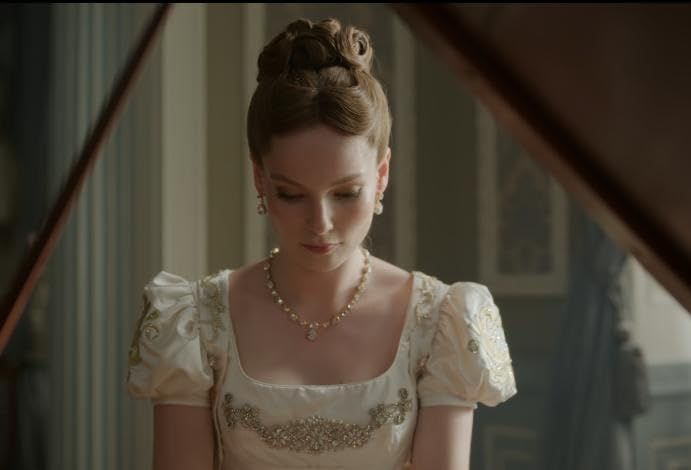 a woman sitting at a piano wearing a white dress and pearls in her hair, looking down