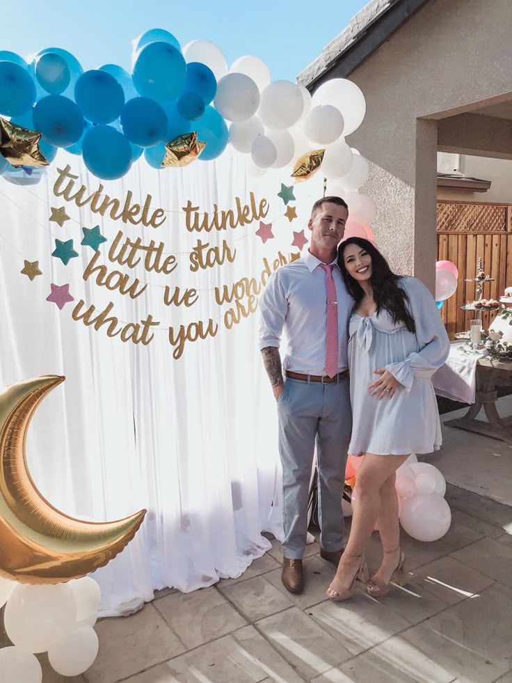 a man and woman standing in front of a backdrop with balloons