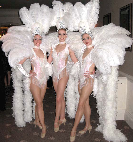 three women dressed in white feather costumes posing for the camera with their arms around each other