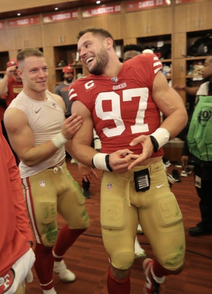 two men in football uniforms standing next to each other on a wooden floor with people watching