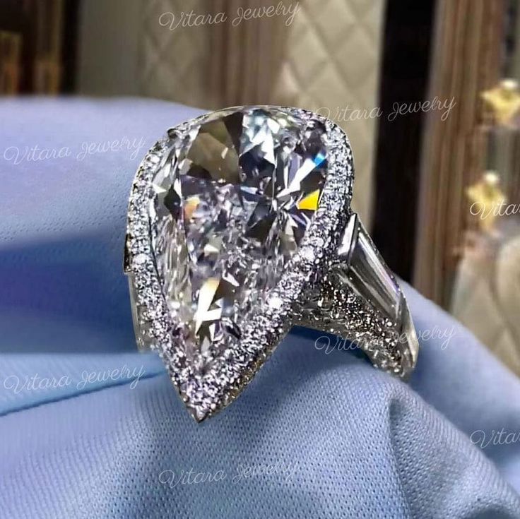 a pear shaped diamond ring with diamonds on it's sides, sitting on a blue cloth