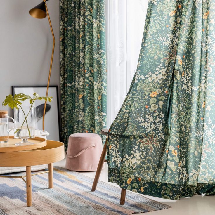 a living room with green curtains and floral print on the drapes, in front of a window