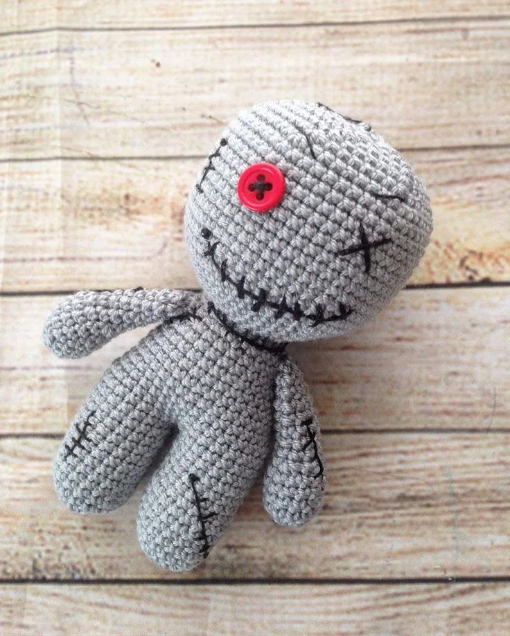 a crocheted gray stuffed animal with a red button on it's head