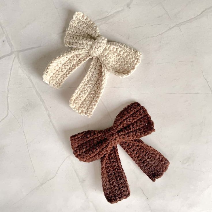 two crocheted bows are sitting on the floor next to each other, one with a bow at the top