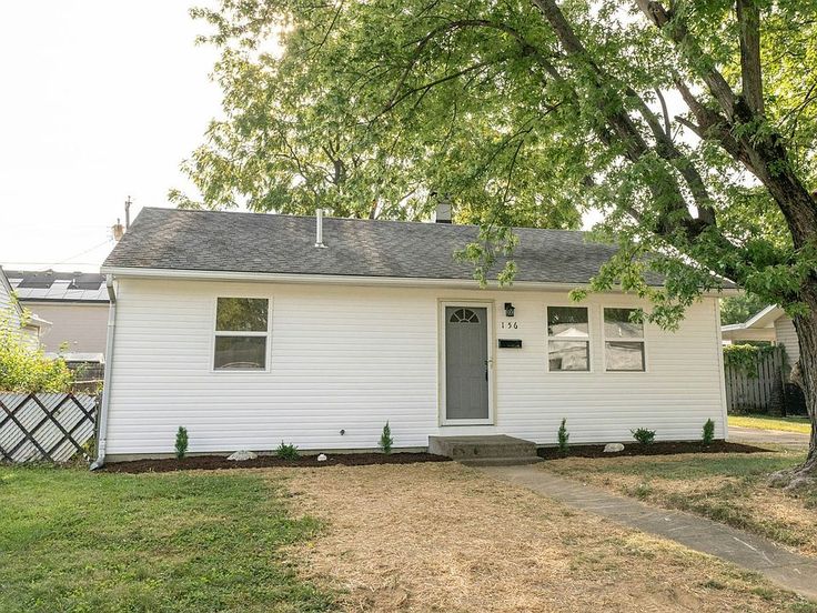 a small white house sitting in the middle of a yard next to a large tree