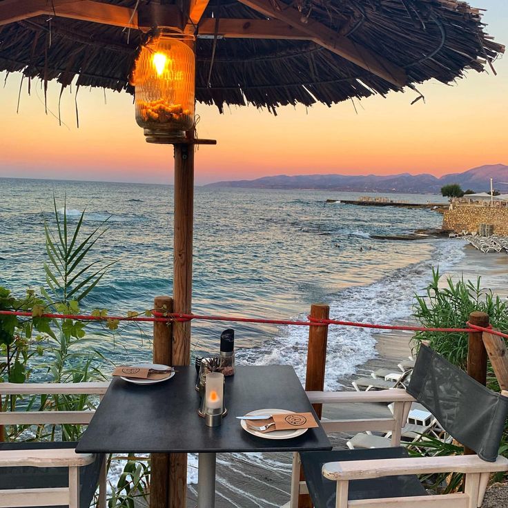 an outdoor dining area overlooking the ocean at sunset with a table and chairs set up for two