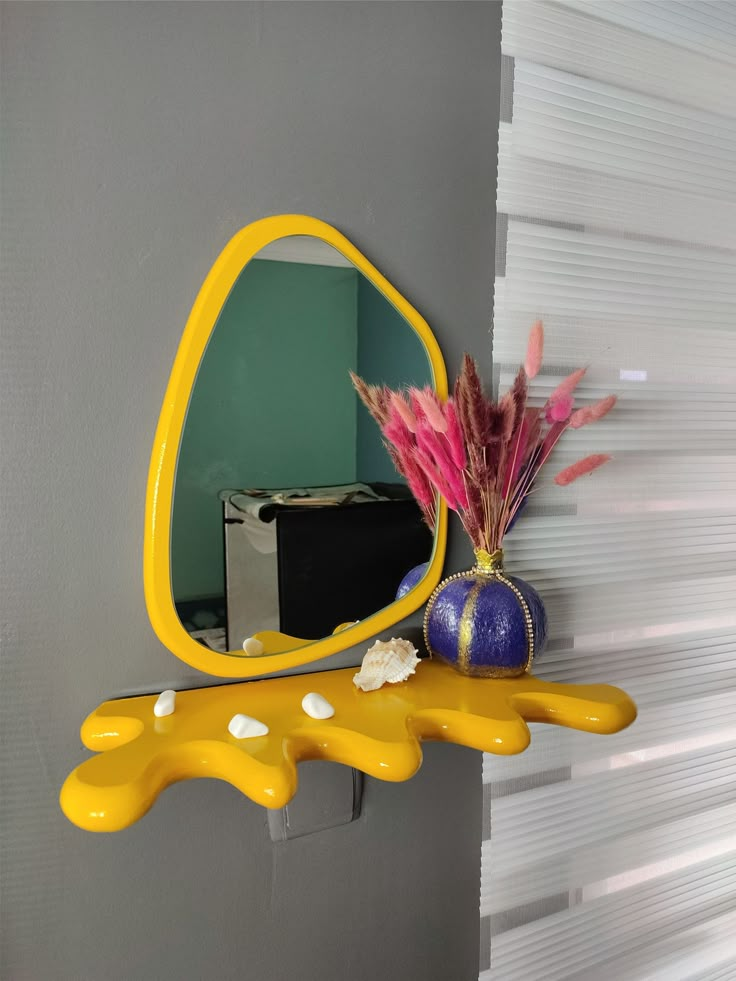 a yellow mirror sitting on top of a wall next to a purple vase