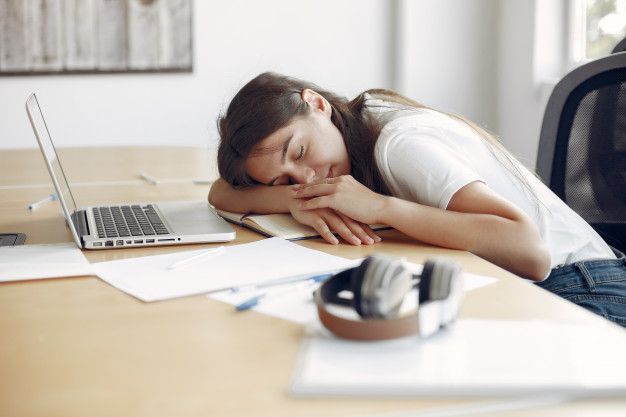 a woman sleeping on her desk next to a laptop