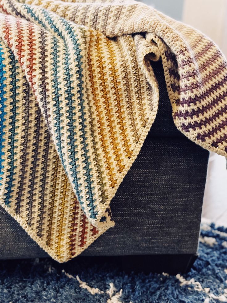 a multicolored blanket sitting on top of a wooden box next to a rug