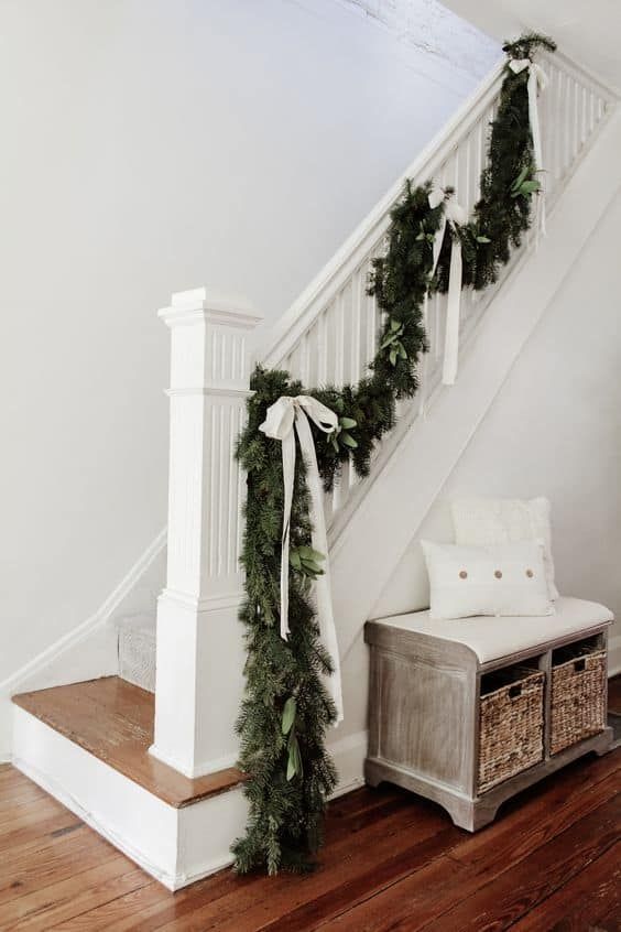 the stairs are decorated for christmas with greenery and bows on them, along with a white bench