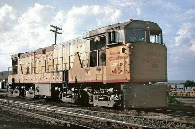 an old train sitting on the tracks in front of some buildings and power lines with clouds in the background