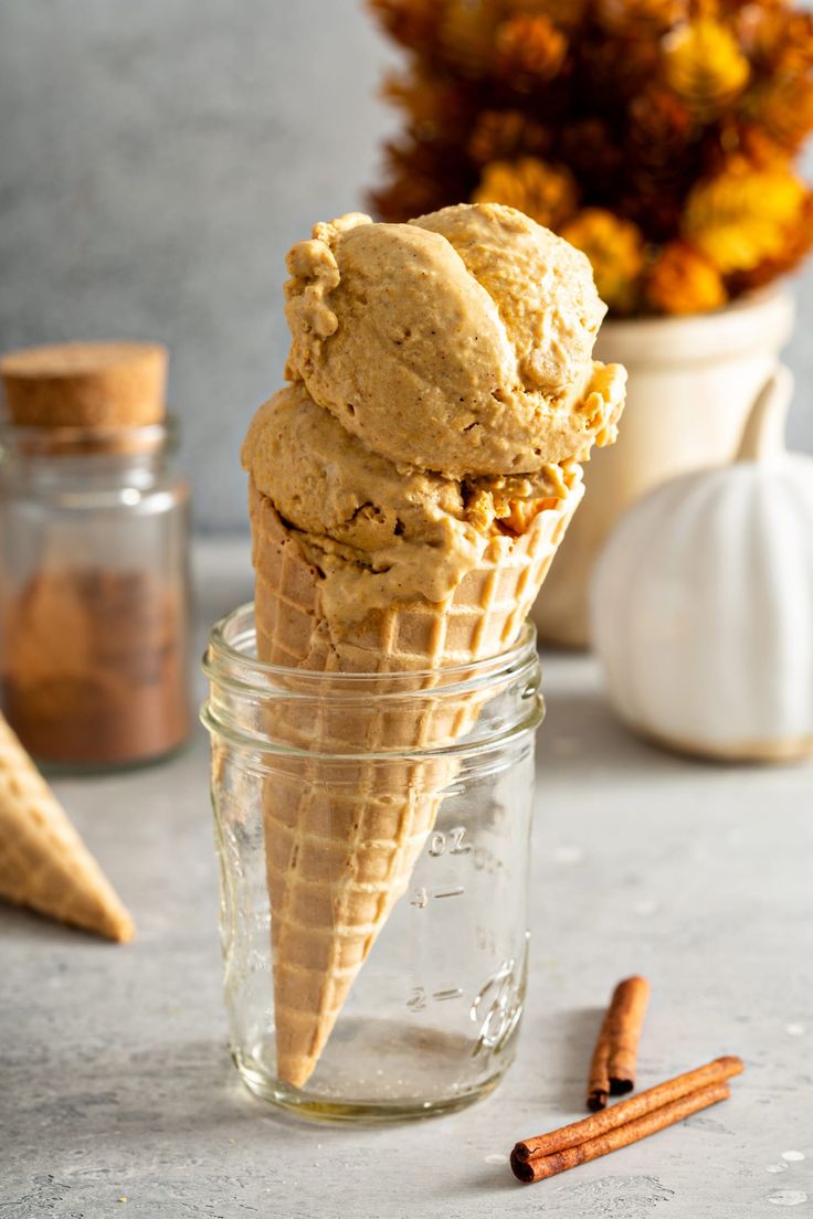 two scoops of ice cream sit in a glass jar next to cinnamon sticks and flowers