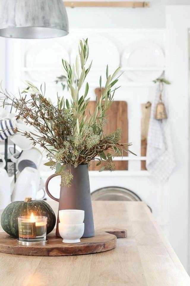 a wooden table topped with a vase filled with greenery and two candles on top of it