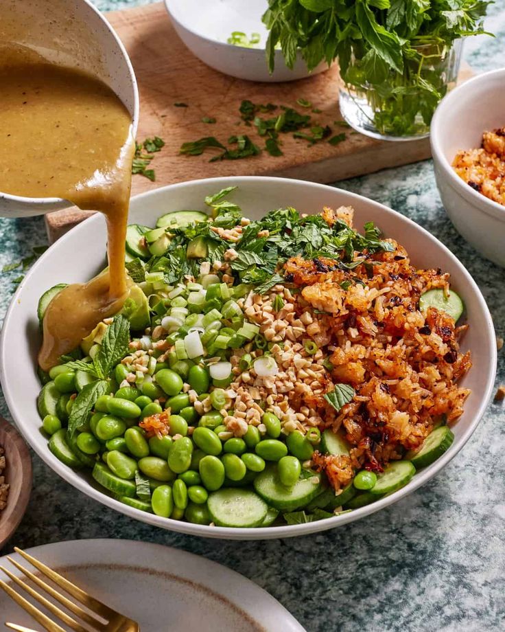 a bowl filled with rice, peas and other vegetables next to two bowls of sauce