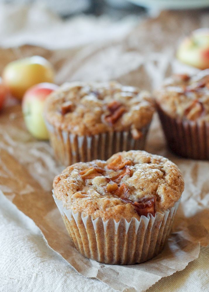 three muffins sitting on top of a piece of wax paper next to apples