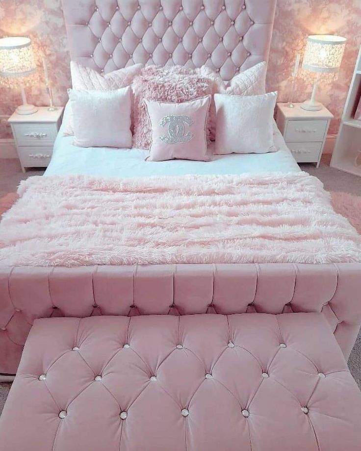 a large pink bed with pillows on it and a foot stool in front of it