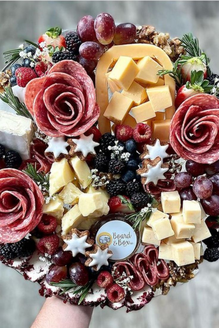 a close up of a person holding a platter with cheese and fruit on it