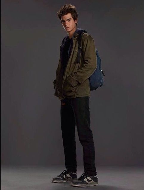 a young man with a backpack standing in front of a gray background and looking at the camera