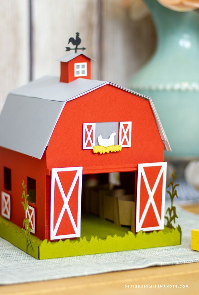 a paper model of a red barn with a gray roof and two white birds on top