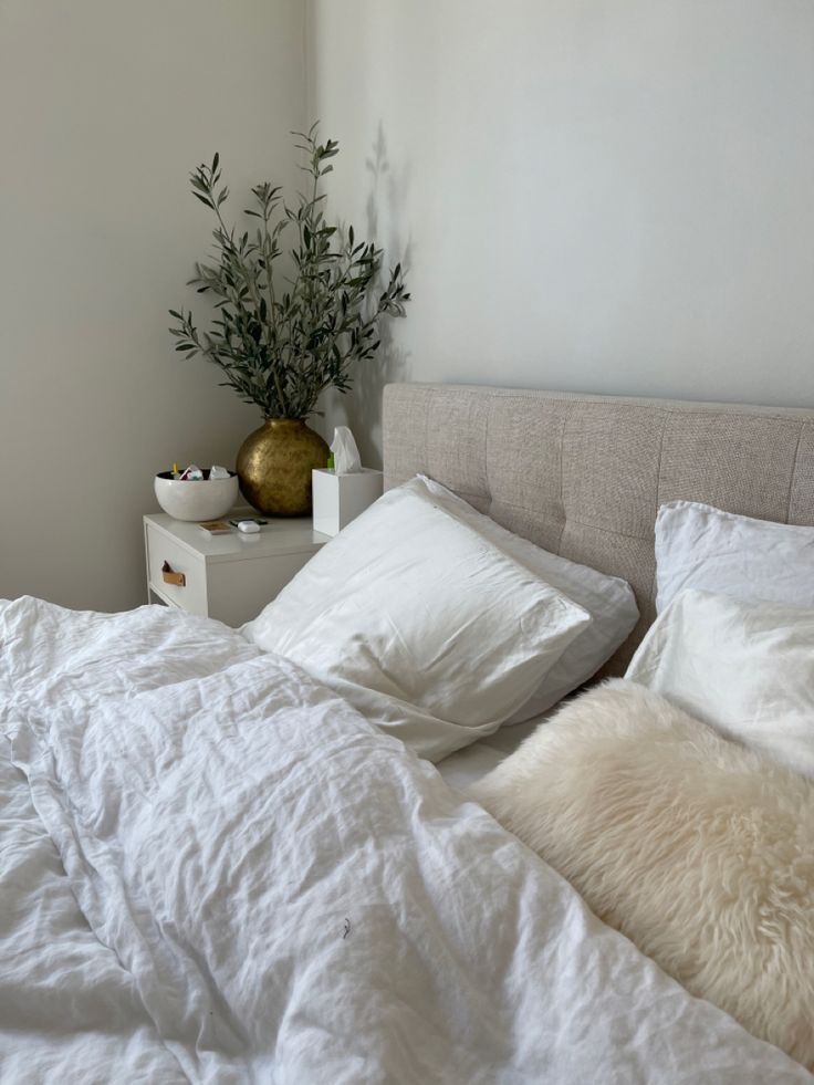 an unmade bed with white sheets, pillows and a plant on the nightstand next to it