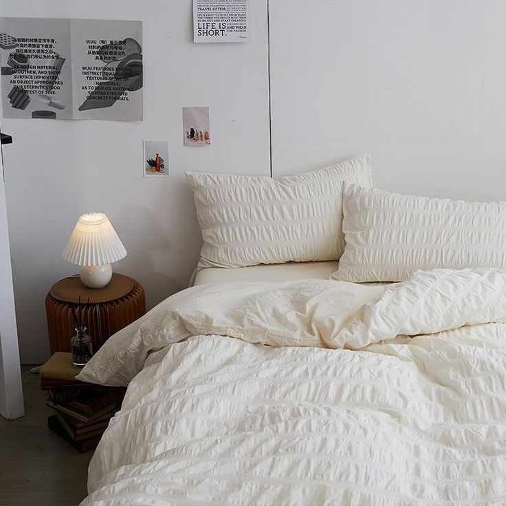 an unmade bed with white comforter and pillows in a small room next to a night stand