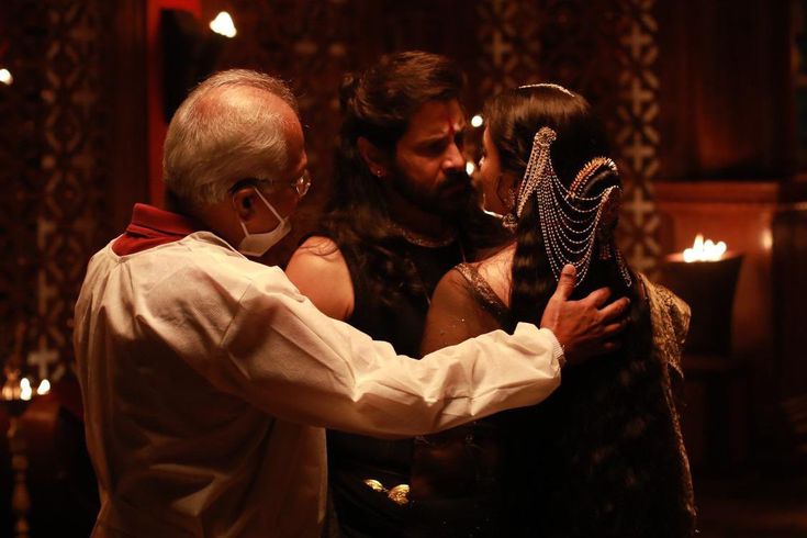 an older man and woman embracing each other in a dimly lit room with candles on the walls