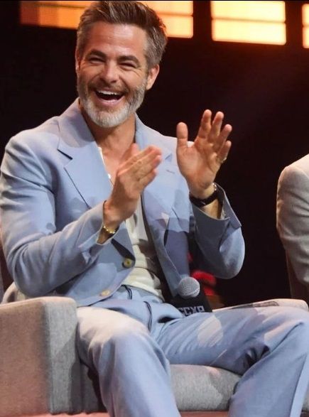 two men in suits sitting on chairs and one is clapping his hands to the side